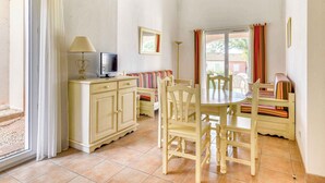 Un coin repas avec une table et des chaises, un téléviseur posé sur un meuble, et une fenêtre avec des rideaux.