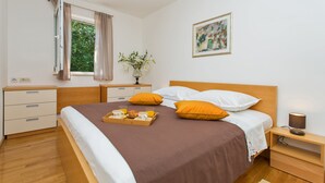 Une chambre à coucher bien rangée, avec un lit, des tables de chevet, une commode, une fenêtre avec des rideaux, un tableau au mur et un plateau contenant des éléments pour le petit-déjeuner.