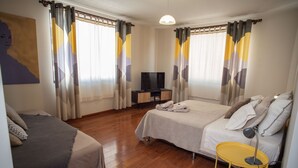 A hotel room with two beds, a television, a yellow side table, and a large window with curtains. - Yellow Gem Apt - Campoverde (Cochabamba)
