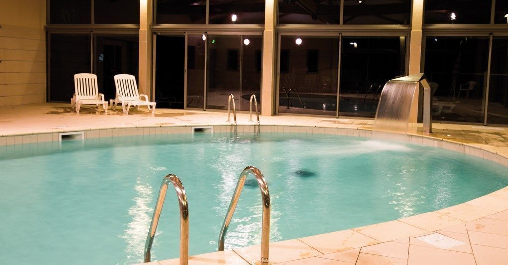 A swimming pool with metal ladders, white lounge chairs, and a waterfall feature.