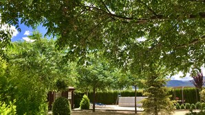 Un jardín con un pérgola de madera, diversos arbustos y un pequeño edificio.