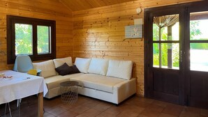 Interior acogedor de una cabaña con pared de madera, un sofá blanco, una mesita y una ventana.