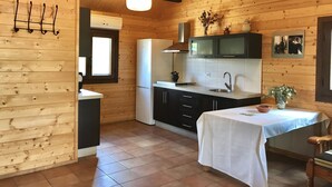 Cocina compacta con paredes de madera, un refrigerador blanco, un lavamanos y una mesa de comedor con mantel blanco.