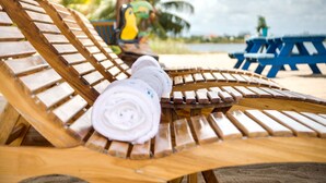 A wooden lounge chair with a rolled-up towel on it, a blue table, and a colorful bird-shaped chair in the background. - Economy Studio beachfront with swim up pool bar (Placencia)