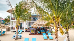 A beachside resort with lounge chairs, palm trees, and a thatched-roof bar area. - Economy Studio beachfront with swim up pool bar (Placencia)