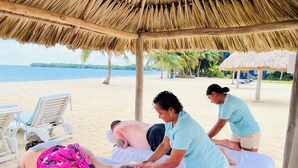 A beachside massage area with a thatched roof, massage tables, and a view of the sea. - Economy Studio beachfront with swim up pool bar (Placencia)