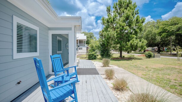 Een huis met een veranda, blauwe stoelen en een pad dat naar de ingang leidt.