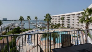 Varanda de hotel com vista para um porto de iates, piscina e palmeiras.