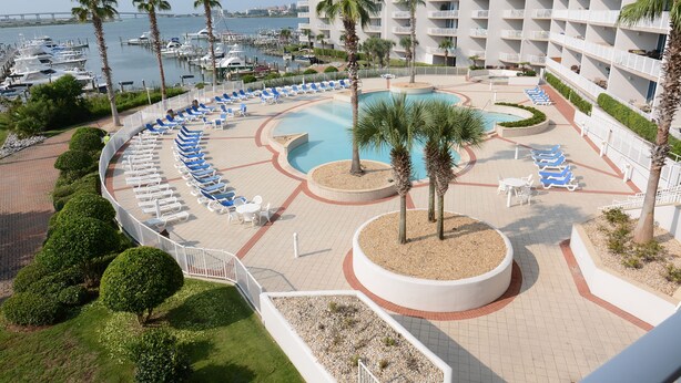 Resort com piscina, cadeiras de descanso, palmeiras e um porto esportivo ao fundo.