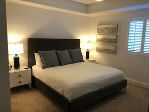 Une chambre à coucher comprenant un lit, deux tables de chevet avec des lampes, une petite table et trois tableaux accrochés au mur.
