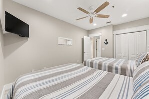 Un dormitorio con dos camas, ventilador de techo, televisor, espejo y armario.