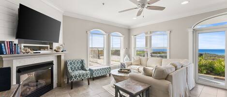 A living room with a fireplace, television, sofa, and large windows with a view.