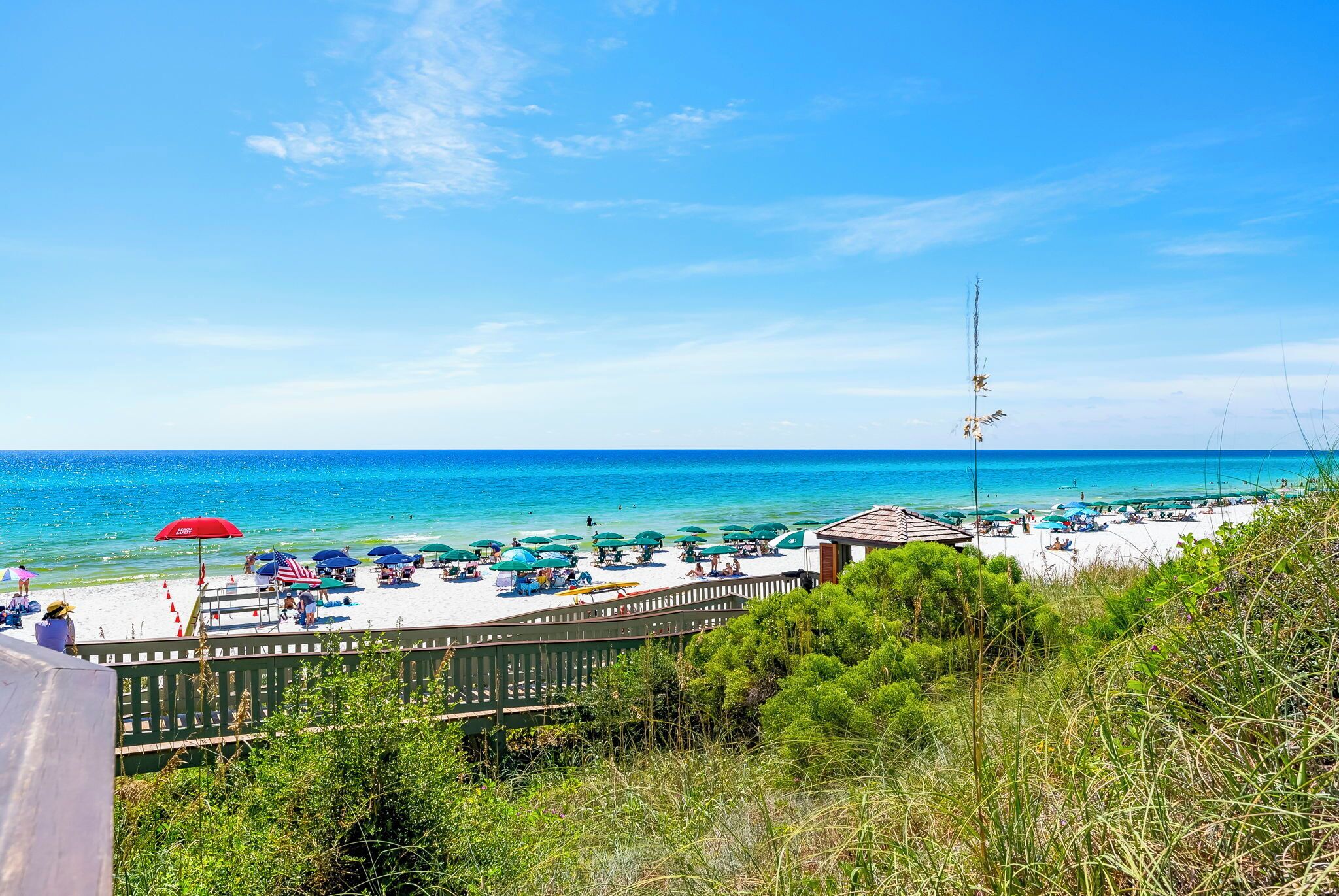 A beach with umbrellas, a wooden fence, and a view of the ocean.