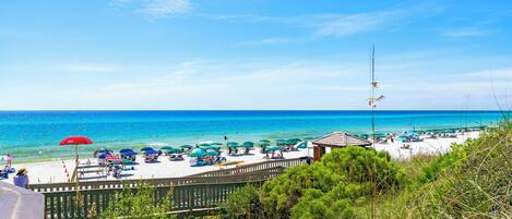 A beach with umbrellas, a wooden fence, and a view of the ocean.