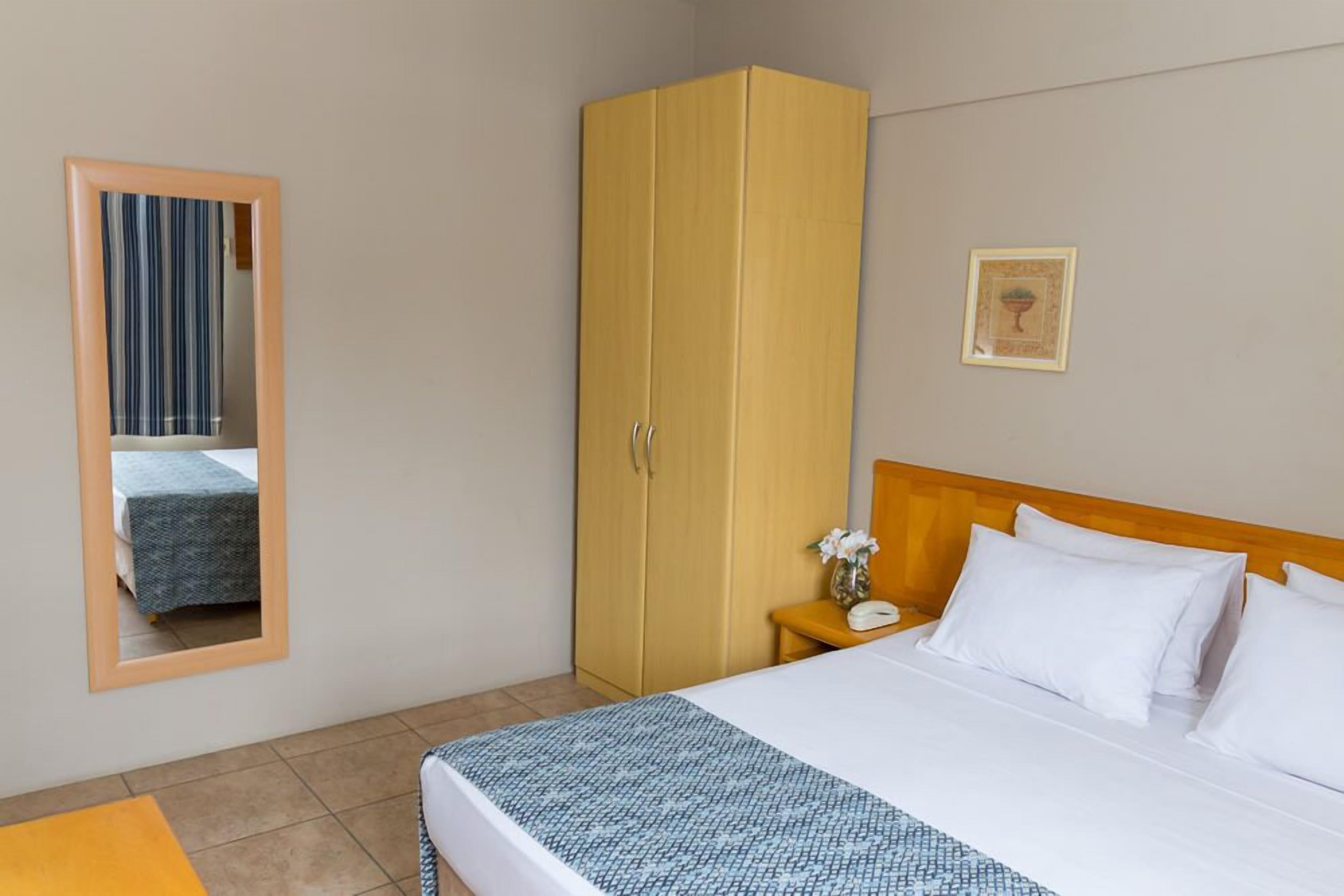 Habitación de hotel con cama, armario, mesita de noche con un florero y un cuadro en la pared.