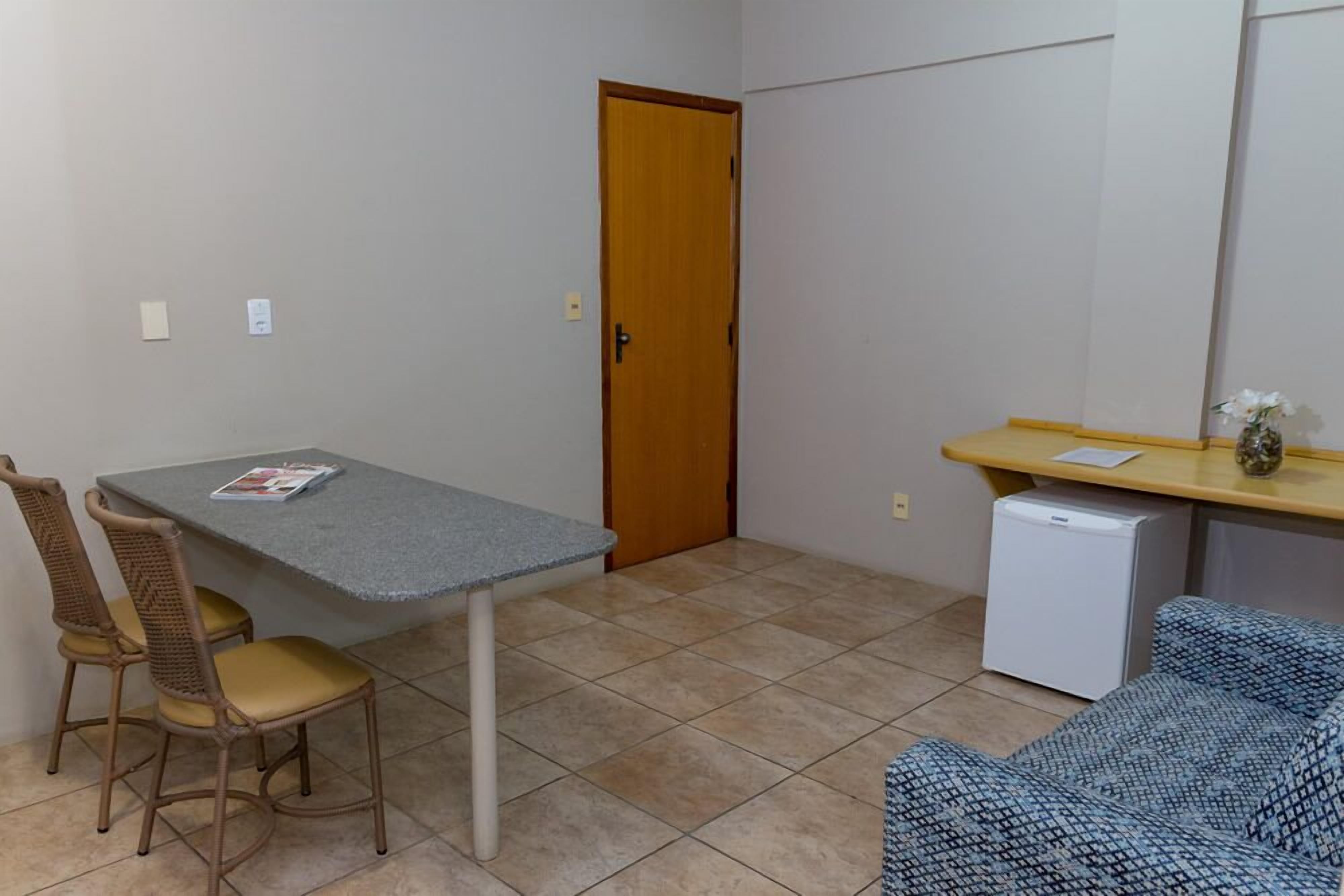 A small room with a table, two chairs, a refrigerator, and a door.