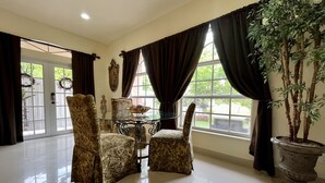 A spacious room with a large window, two patterned armchairs, a glass-top table with a decorative bowl, and a potted plant.