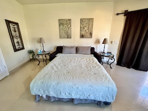 A spacious bedroom with a large bed, two side tables, a potted plant, and artwork on the walls.