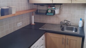Een kleine keuken met een wasmachine, een spoelbak en houten keukenkastjes.