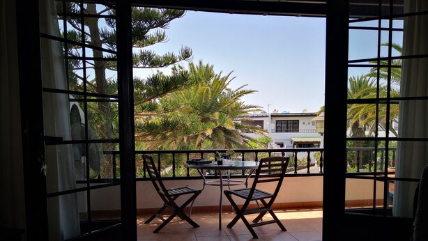 Een balkon met twee stoelen en een tafel, met uitzicht op een woonwijk met palmbomen en huizen.