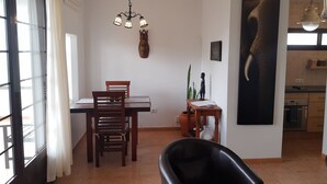 Een eetgedeelte met een tafel, stoelen, een zwarte leren fauteuil, een wandsculptuur en een keuken op de achtergrond.