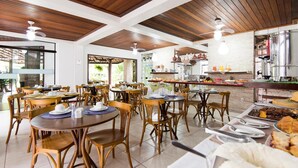 Un restaurant avec des tables et des chaises en bois, un buffet proposant divers plats et un espace cuisine.