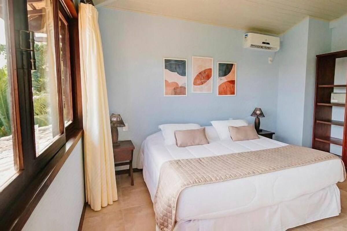 Une chambre à coucher avec un lit, une table de chevet, une lampe, une armoire et une fenêtre avec des rideaux.