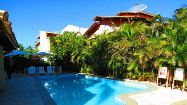 Une piscine à bordures courbes, entourée de palmiers et bordée d’un bâtiment doté d’une antenne parabolique.