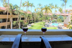 A balcony with two wine glasses, overlooking a pool area with palm trees and a golf course. - Large condo w/ 2 suites, 60ft terrace, grill, 1blk to beach/2 blk to downtown  (Cabo San Lucas)