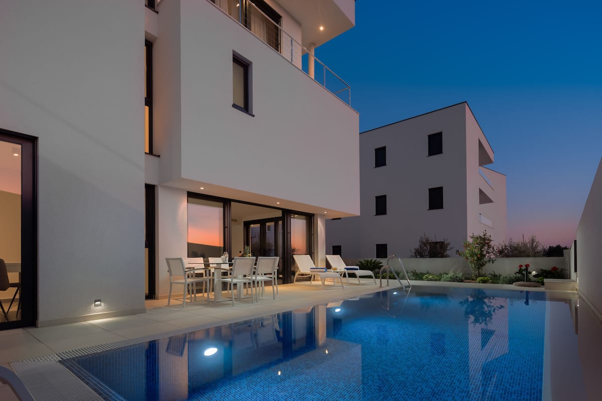 Un área de piscina moderna con sillones de descanso y una zona de comedor.