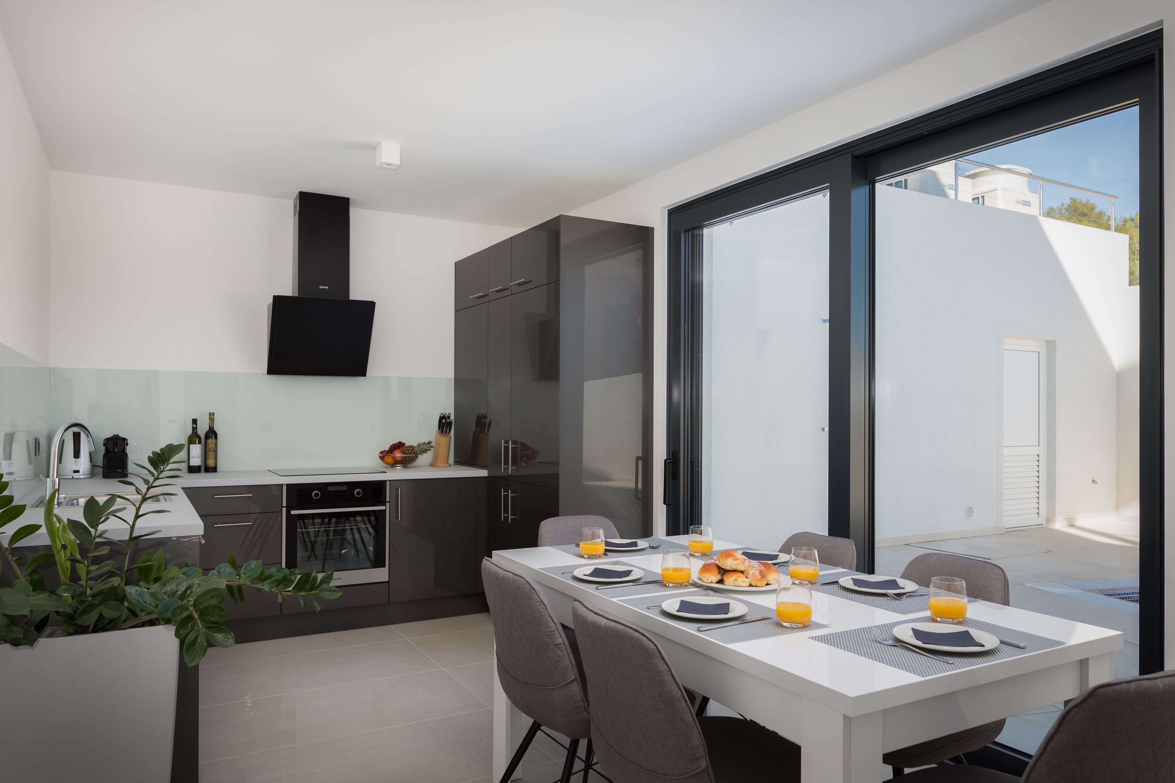 Eine moderne Küche mit Essbereich, großen Fenstern und Ausblick nach draußen.