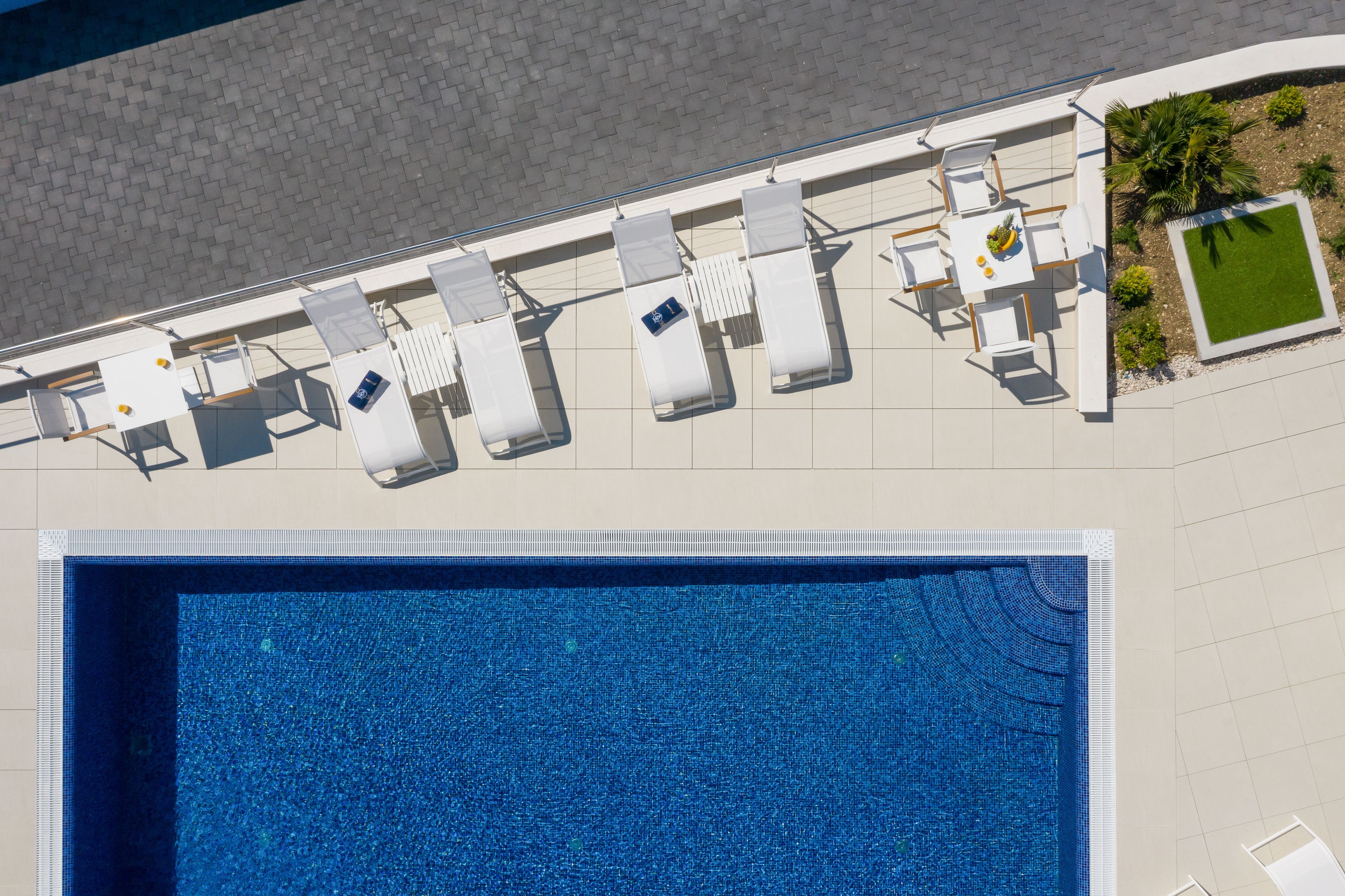 An aerial view of a hotel pool area with lounge chairs and a small garden.