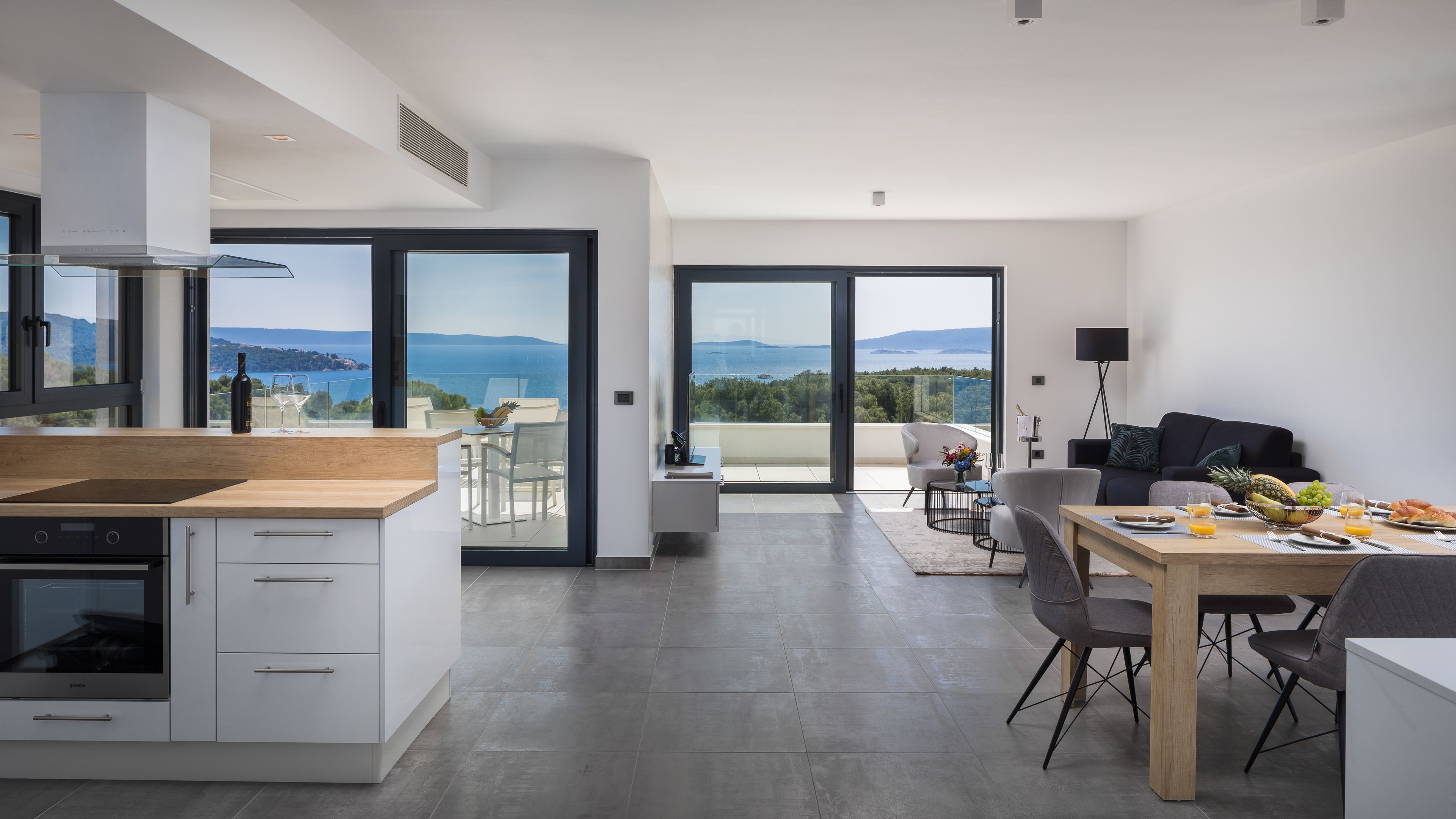 A modern kitchen with a large island, a dining area with a view, and a living space with a sofa and a coffee table.