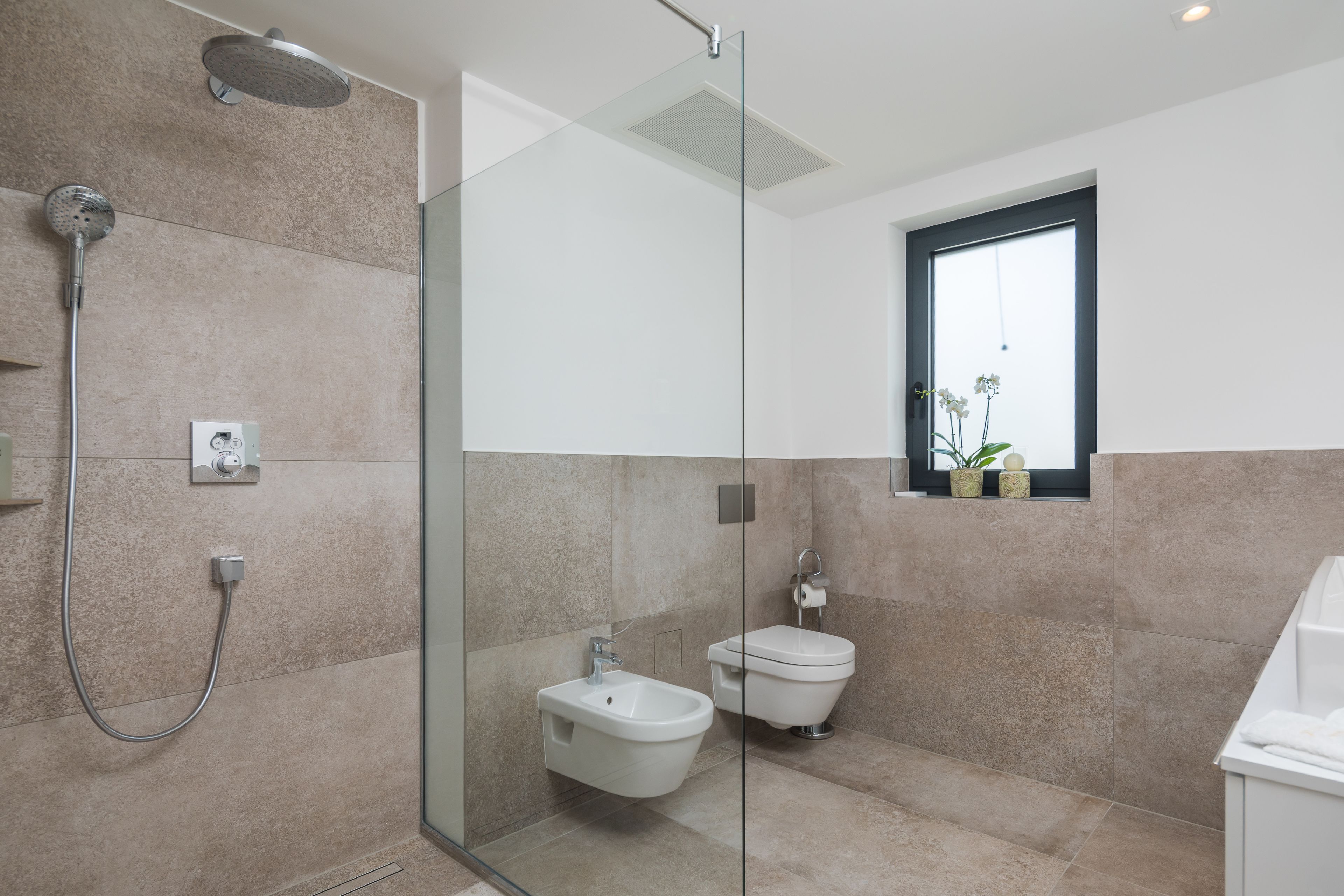 A modern bathroom with a glass shower enclosure, a bidet, and a toilet.