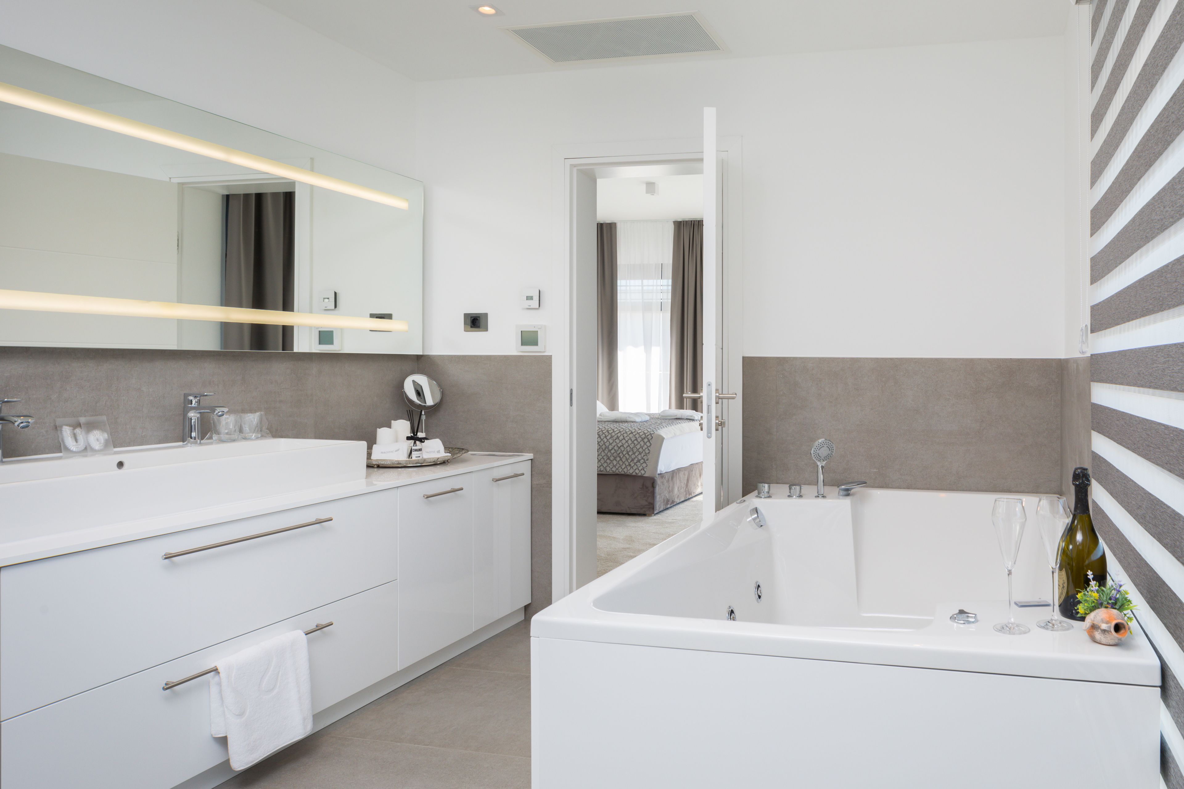 A modern bathroom with a large mirror, white vanity, and a bathtub.