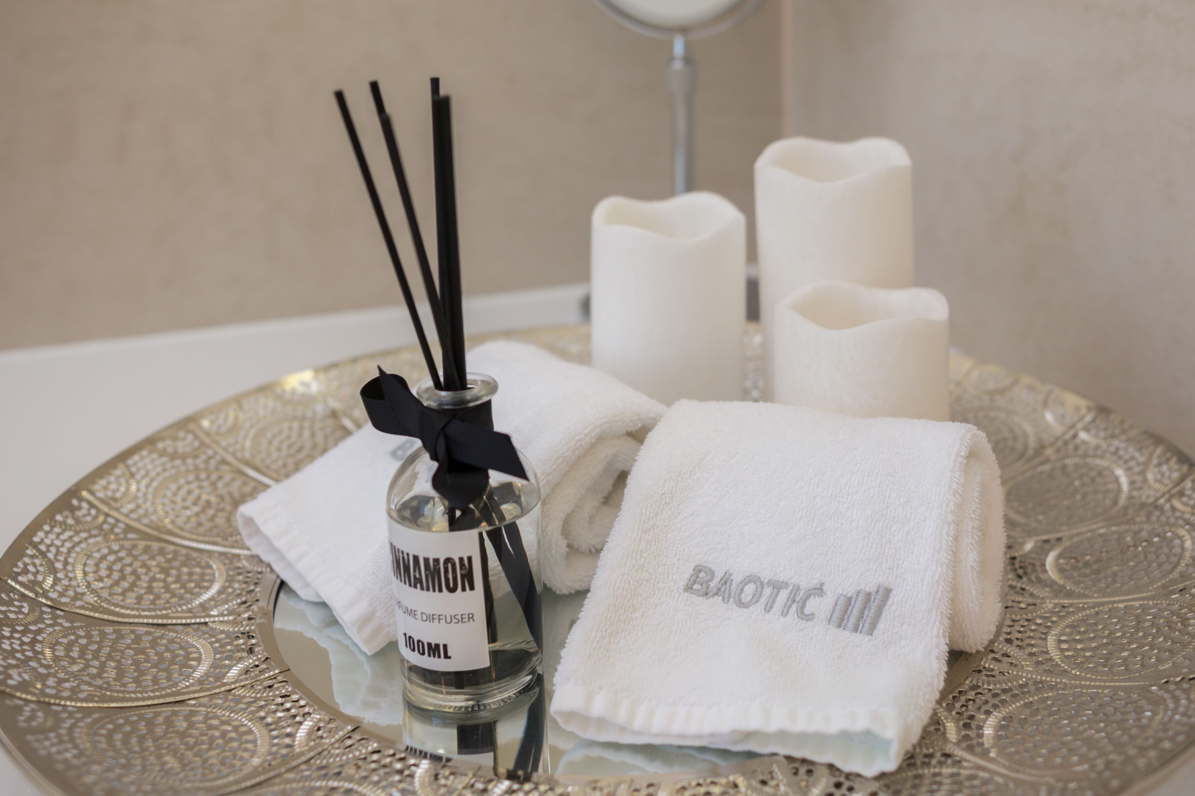 A tray with a bottle of "CINNAMON" fragrance, white towels, and candles.