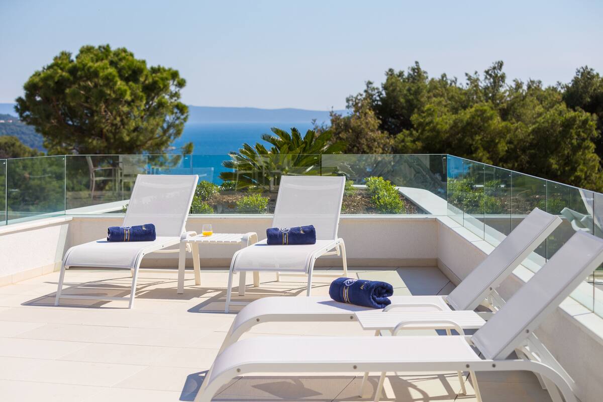 Una terraza con sillones blancos, barandilla de vidrio y vista al mar.