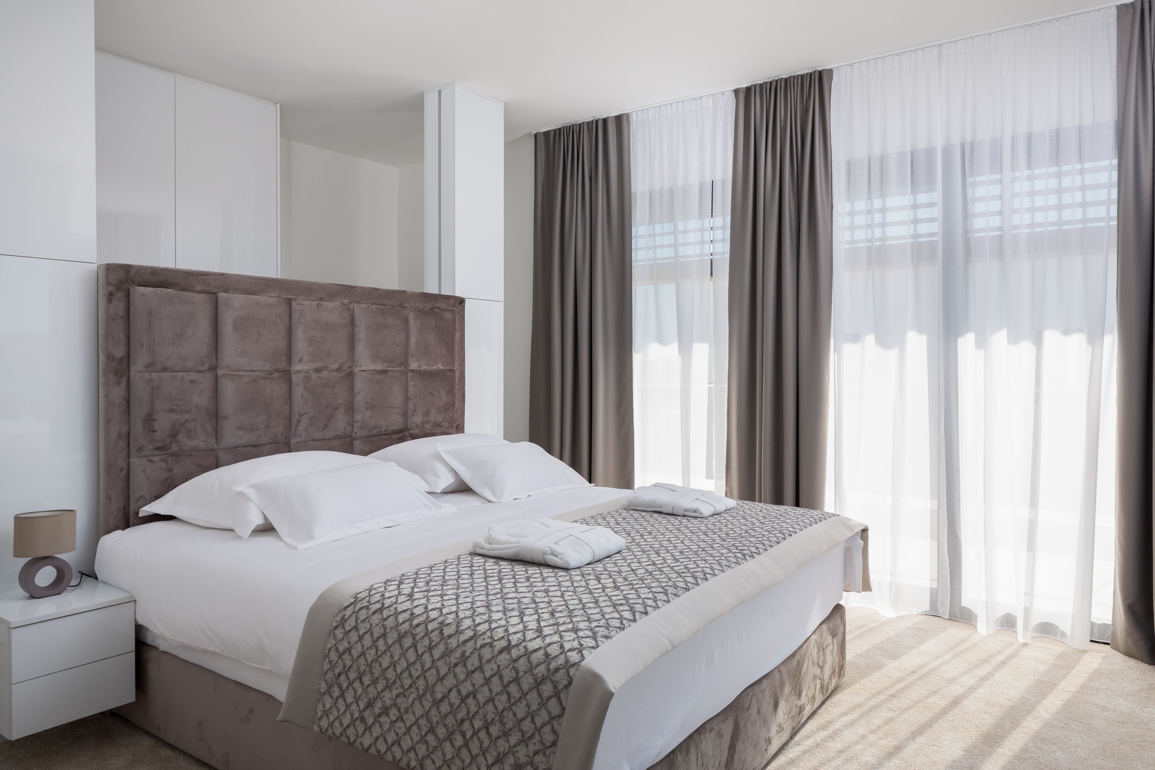Une chambre d’hôtel moderne avec un grand lit, une tête de lit, une table de chevet et une fenêtre avec des rideaux.
