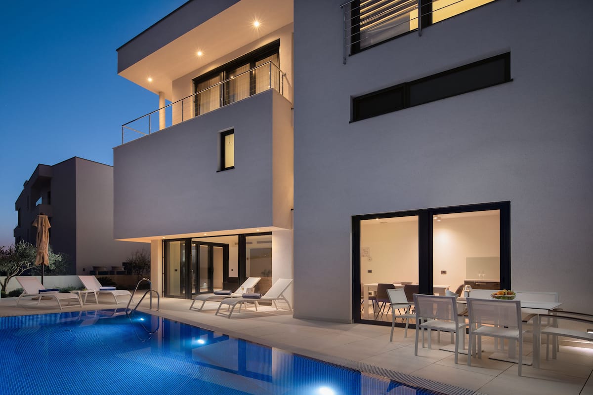 Un edificio moderno de dos pisos con piscina, sillas de descanso y zona de comedor.