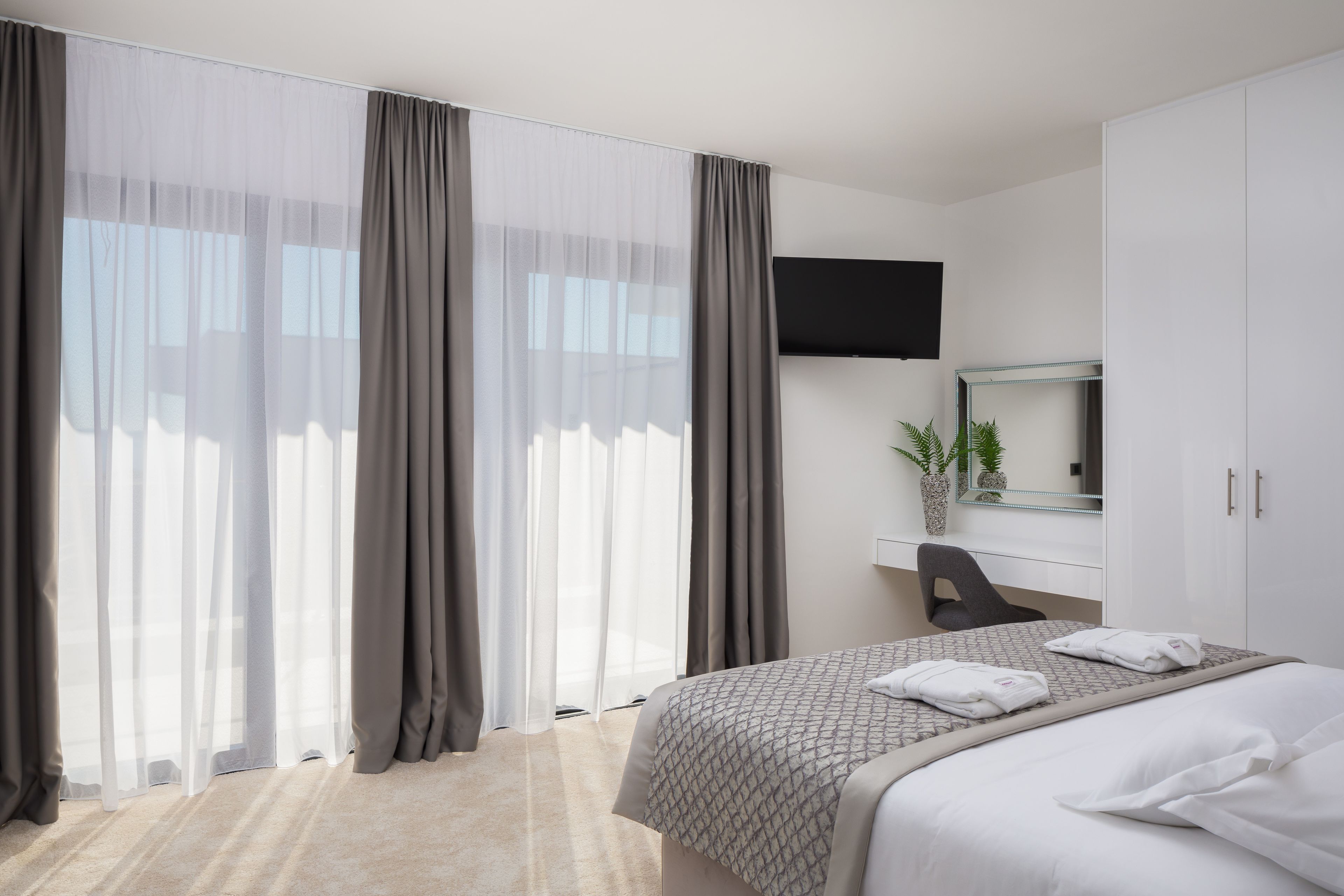 A hotel room with a bed, a desk, a chair, a TV, and a large window with curtains.