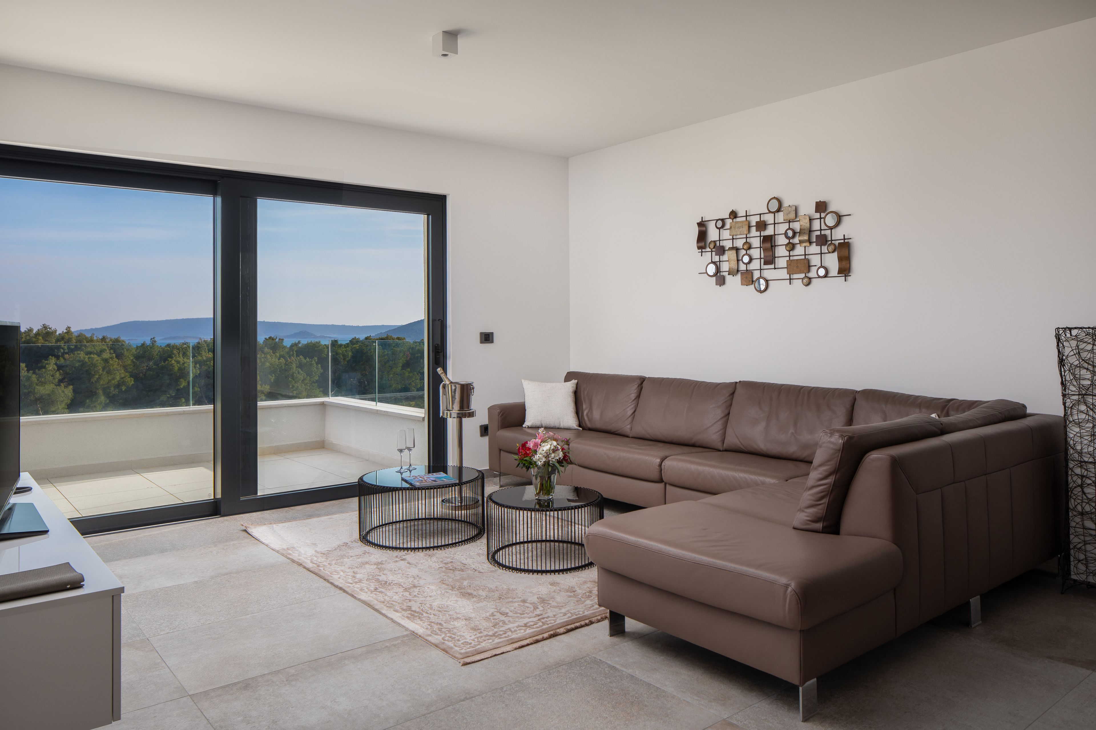 Ein modernes Wohnzimmer mit einer Couch, zwei Couchtischen, einer Wanddekoration und Blick ins Freie.