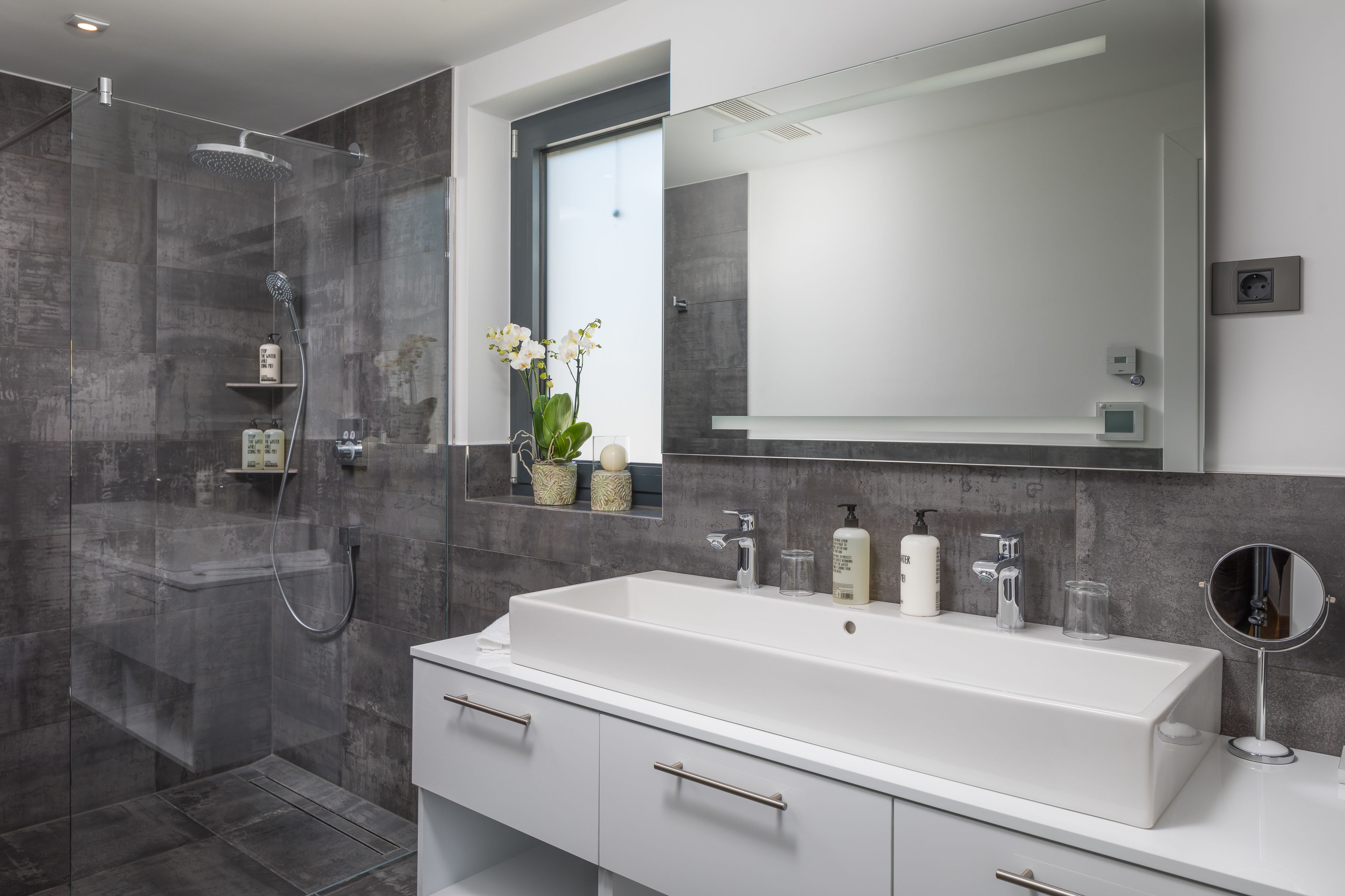 Een moderne badkamer met een groot wit wastafelmeubel, een douche met glazen wanden en een grote spiegel.
