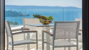 A table with a fruit bowl and two white chairs with wooden accents, overlooking a scenic view of the sea. - Villas Baotic (Seget)