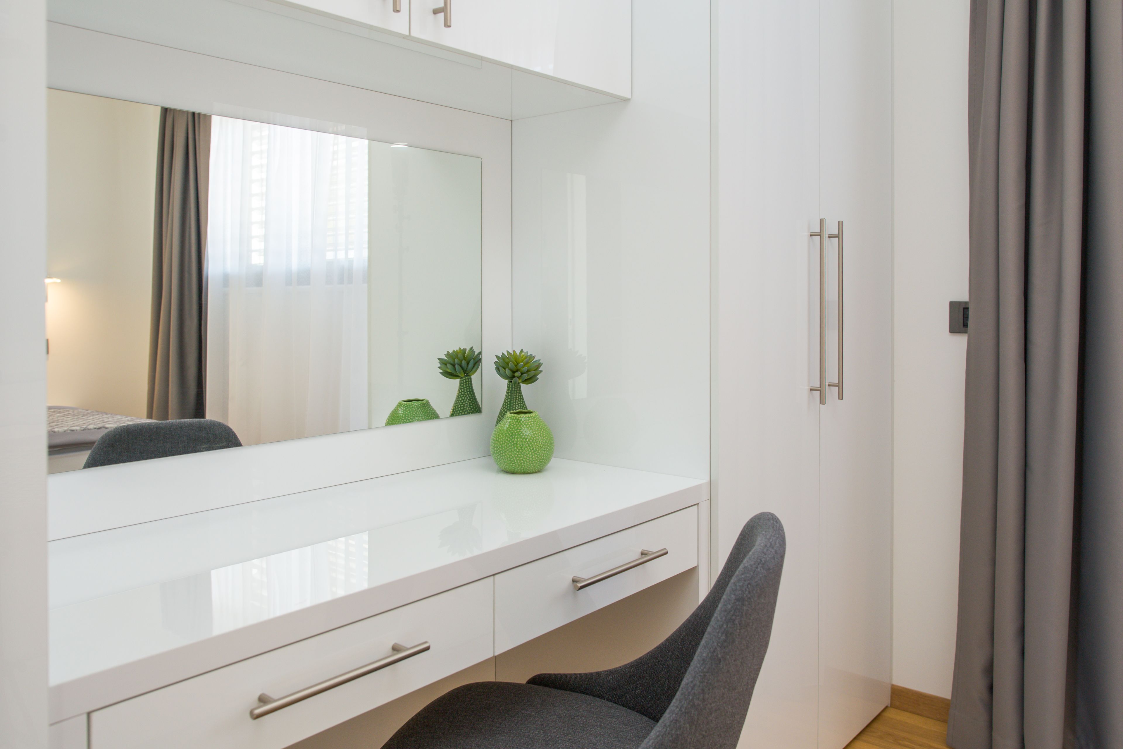 A modern room with a white vanity, a mirror, a chair, and a small green plant.