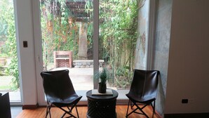 Ein Zimmer mit zwei schwarzen Ledersesseln, einem kleinen runden Tisch und Blick auf einen Garten durch eine große Schiebetür.
