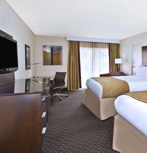 A hotel room with a bed, a desk, a chair, a television, and a window with curtains.