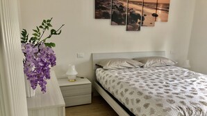 Ett sovrum med en säng, ett nattduksbord, en lampa, en vas med blommor och en vägg med en tavla.