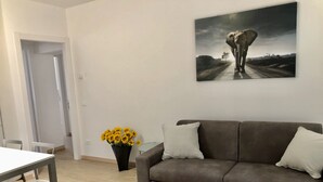 Ett vardagsrum med en brun soffa, ett matbord med stolar, en vas med gula blommor och en tavla med en elefant på väggen.