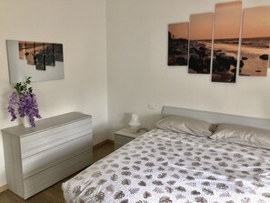 Une chambre à coucher comprenant un lit, une commode, une table de chevet, une lampe et des œuvres d’art murales.