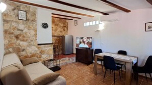 Ein Wohnzimmer mit Steinwand, einem Fernseher, einem Esstisch mit Stühlen und einem Sofa.